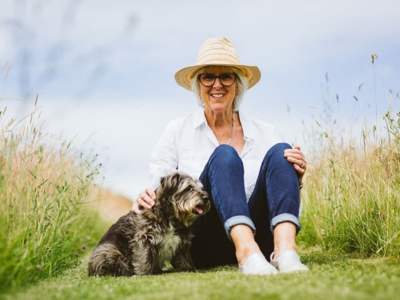 Lavinia, Peaches supporter, sitting on mown lawn with her dog. White female, white short hair, wearing glasses and straw hat, blue jeans