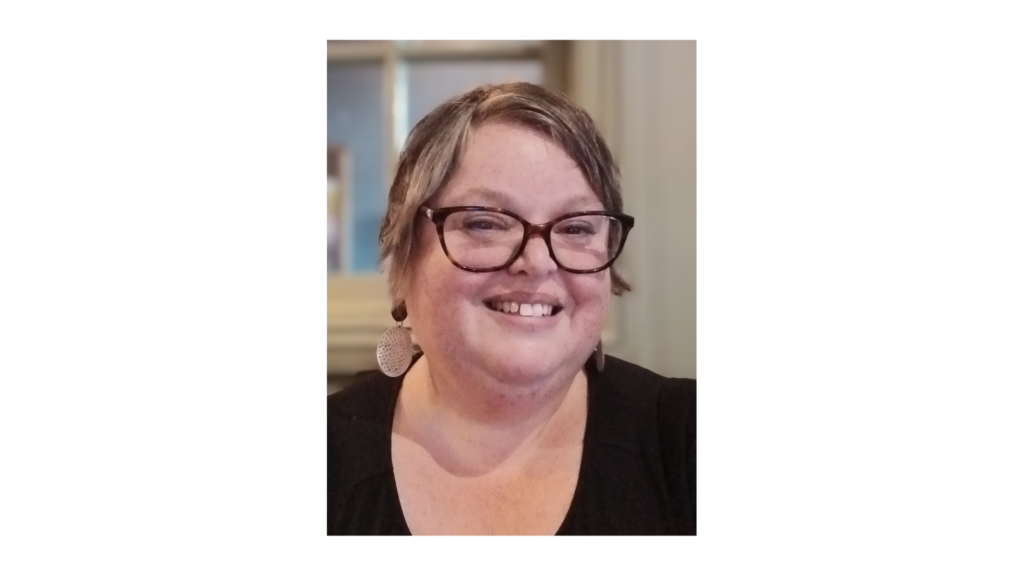 Fay, Peaches supporter, white female with short brown hair, wearing glasses, disc earrings and black top